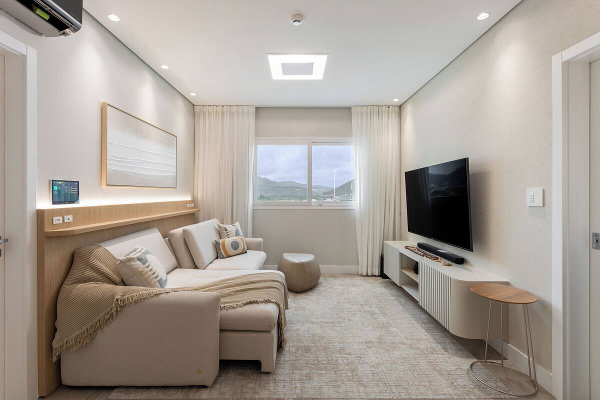 A modern living room with a sofa set, a TV, and a large window with a view of the outdoors.
