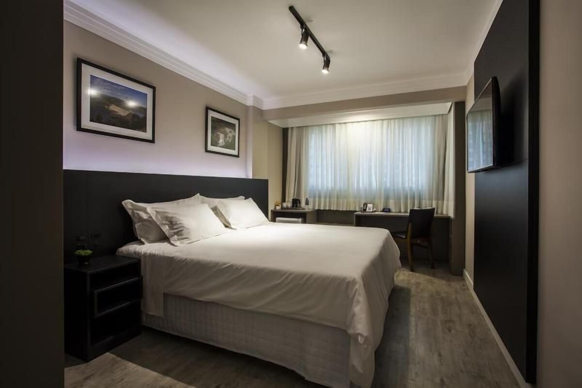 A hotel room with a large bed, bedside tables, a desk, and a chair.
