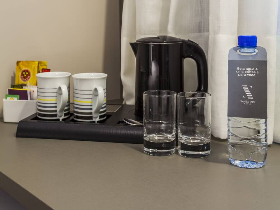 Ontbijt in een hotelkamer, met een dienblad waarop twee witte mokken met strepen, twee glazen, een zwart elektrisch waterkoker, een waterfles en een pakje koffiemelk staan.