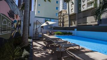 A rooftop pool area with lounge chairs, umbrellas, and a mural on the wall.