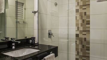 A modern bathroom with a glass shower enclosure, a large mirror, and a black countertop with a sink.