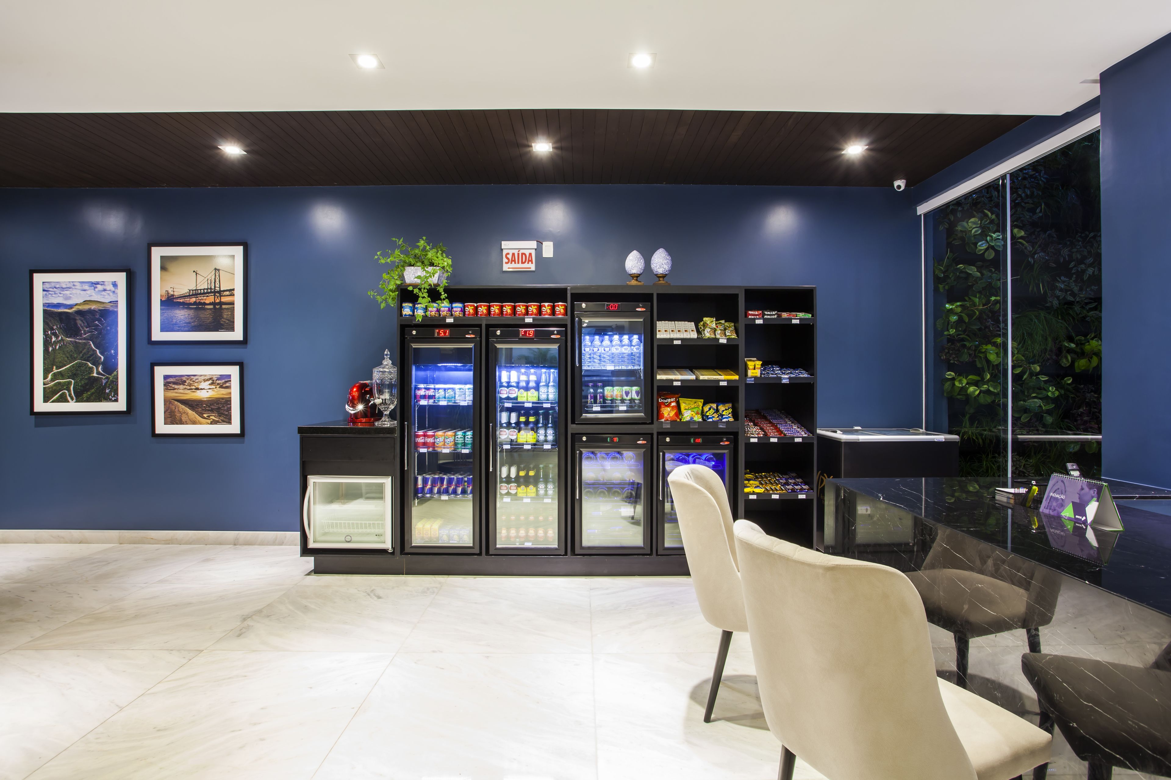 Interior moderno com parede azul, geladeira com bebidas e mesa de vidro com cadeiras.
