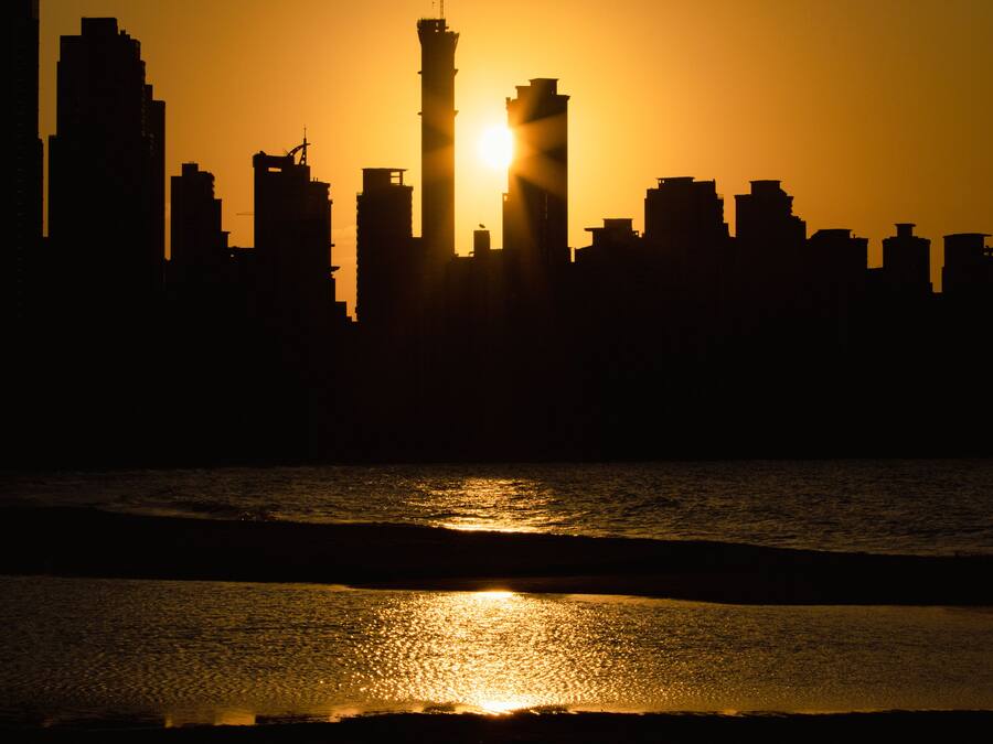 Silueta del horizonte de una ciudad al atardecer, con una masa de agua en primer plano.