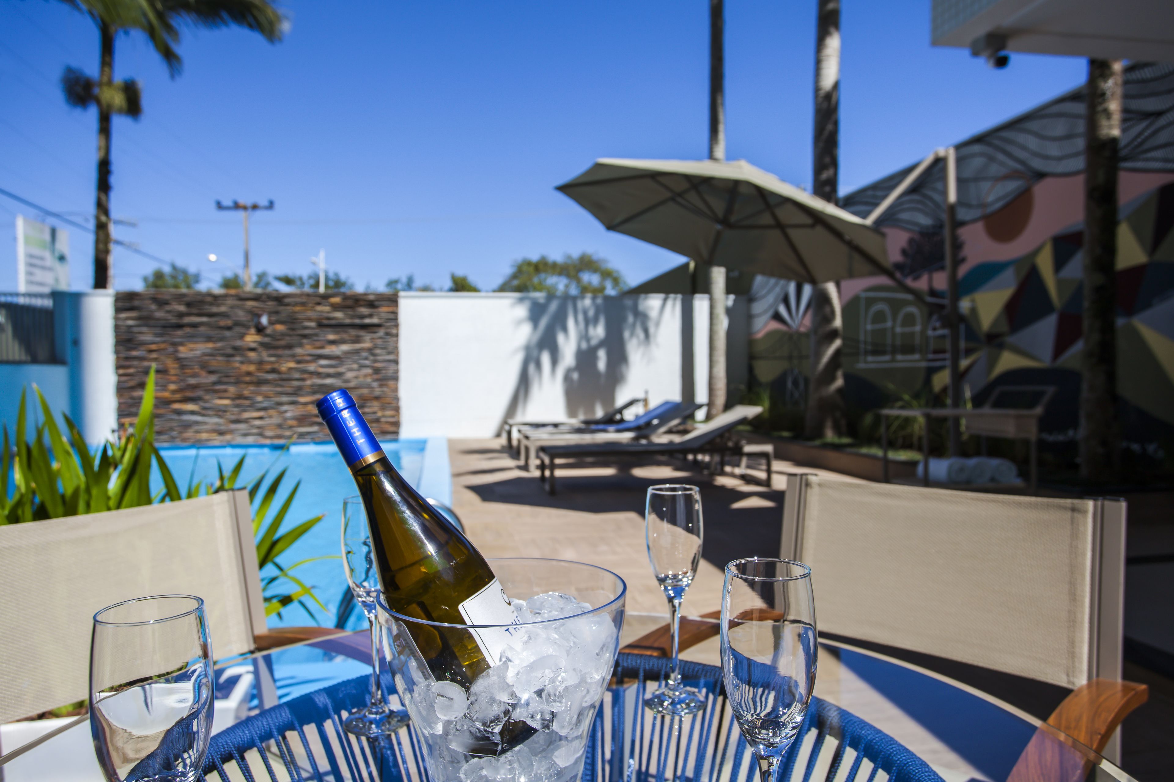Una mesa junto a la piscina con una botella de vino, copas y una tumbona.