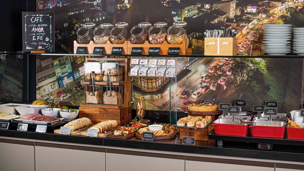 A buffet with various food options and a cityscape view in the background. - Santa Inn Hotel (Balneário Camboriú)
