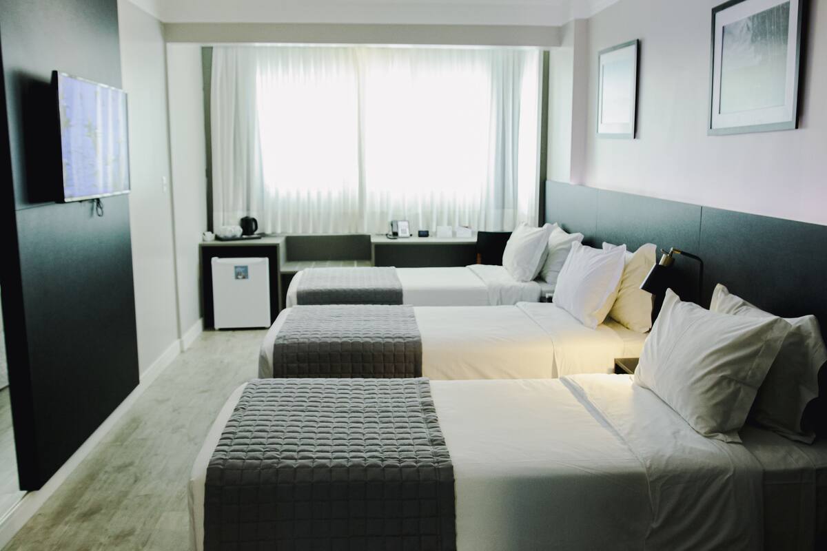 A hotel room with two beds, a desk, a chair, a small table, and a window with curtains.