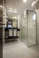 Un baño moderno con ducha de vidrio, tocador negro y espejo sobre el lavabo.