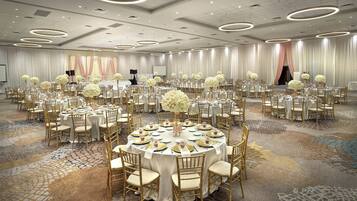 A large banquet hall with round tables, gold chairs, and white tablecloths.