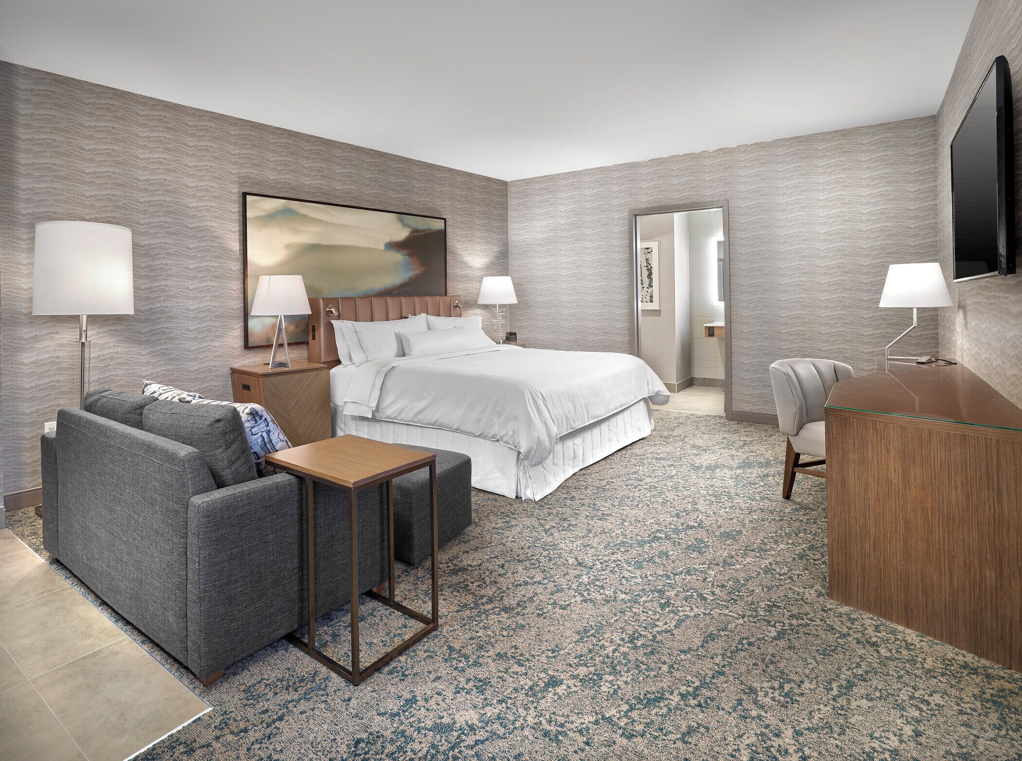 Ett modernt hotellrum med en stor säng, en soffa, ett skrivbord och en TV.