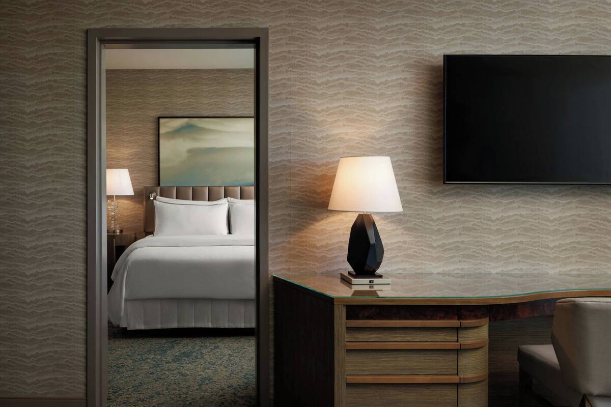 A hotel room with a bed, a desk with a lamp, and a television on the wall.