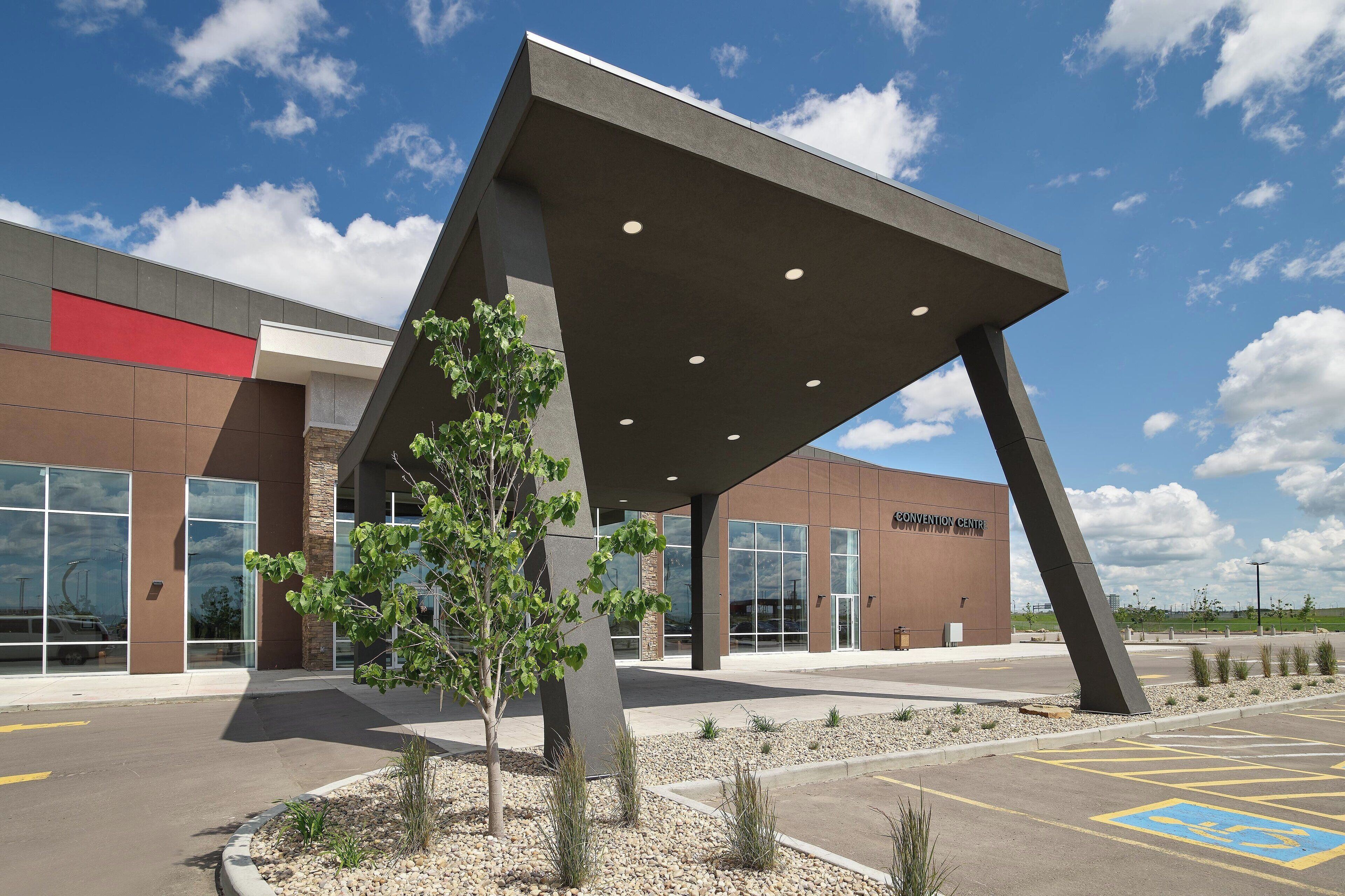 A modern building with a large overhang, a parking lot, and a tree in the foreground.
