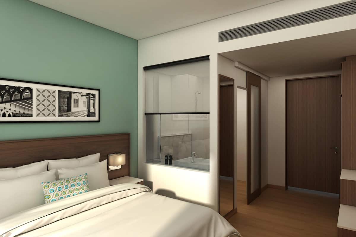 Une chambre d’hôtel moderne, équipée d’un lit, d’une grande fenêtre donnant sur une salle de bain, d’une œuvre d’art accrochée au mur et d’une porte en bois.