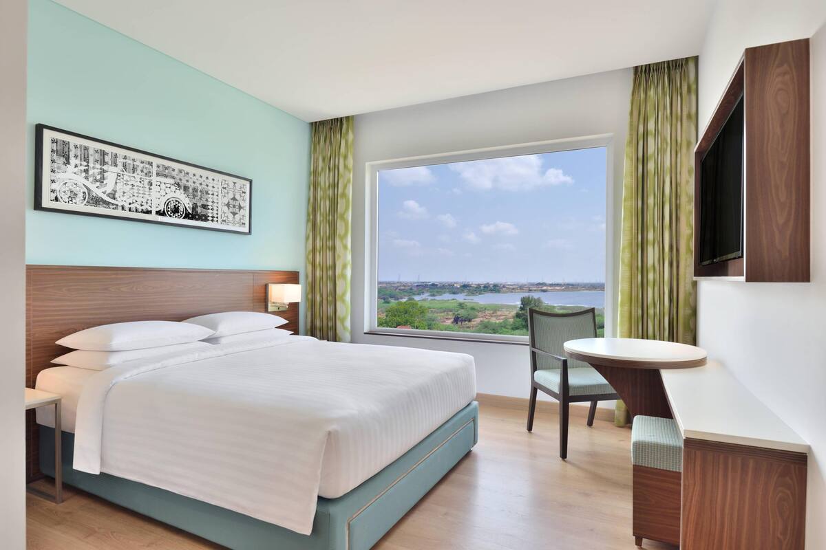 Une chambre d’hôtel équipée d’un lit, d’un bureau, d’une chaise, d’une télévision et d’une fenêtre donnant sur un plan d’eau.