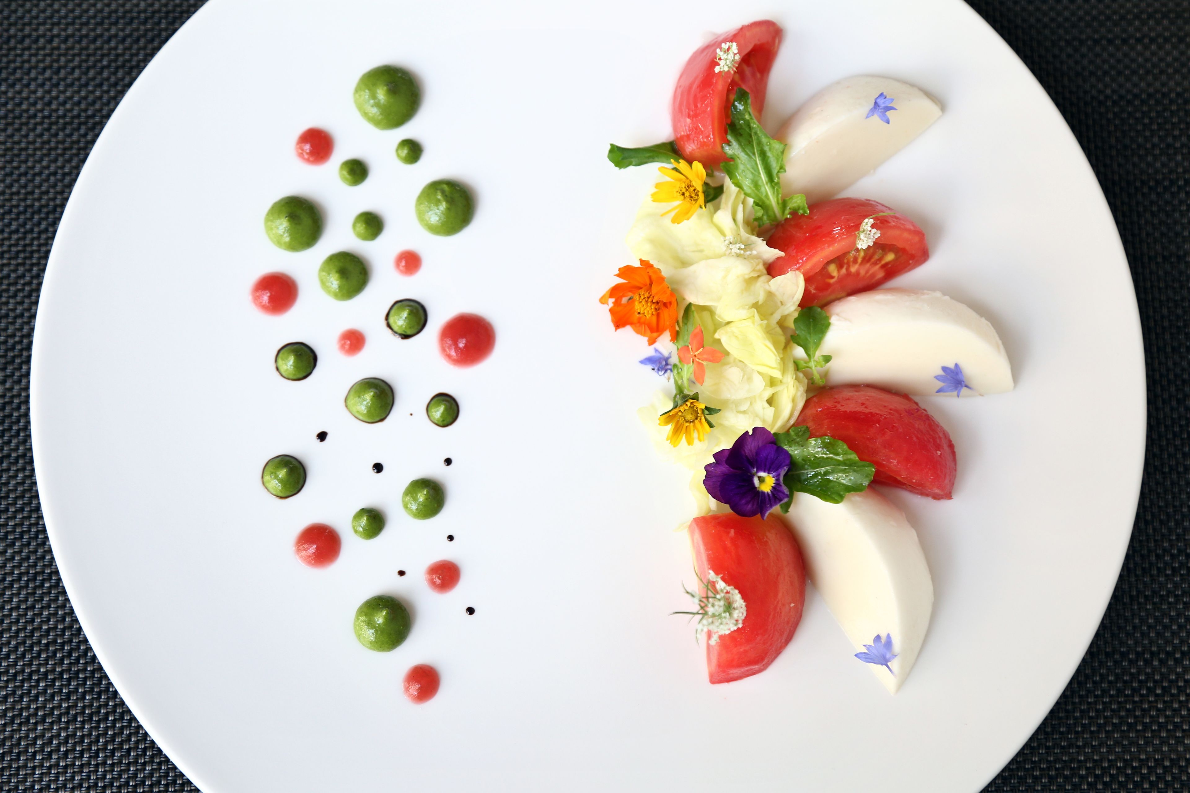 A white plate with a decorative arrangement of tomatoes, flowers, and green spheres.