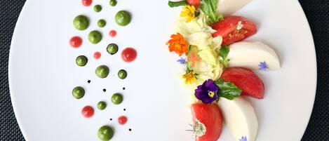 A white plate with a decorative arrangement of tomatoes, flowers, and green spheres.