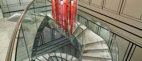A modern spiral staircase with glass railings and a central column, surrounded by a minimalist wall design.