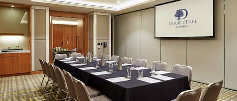 A conference room with a long table, chairs, a projector screen, and a kitchenette.