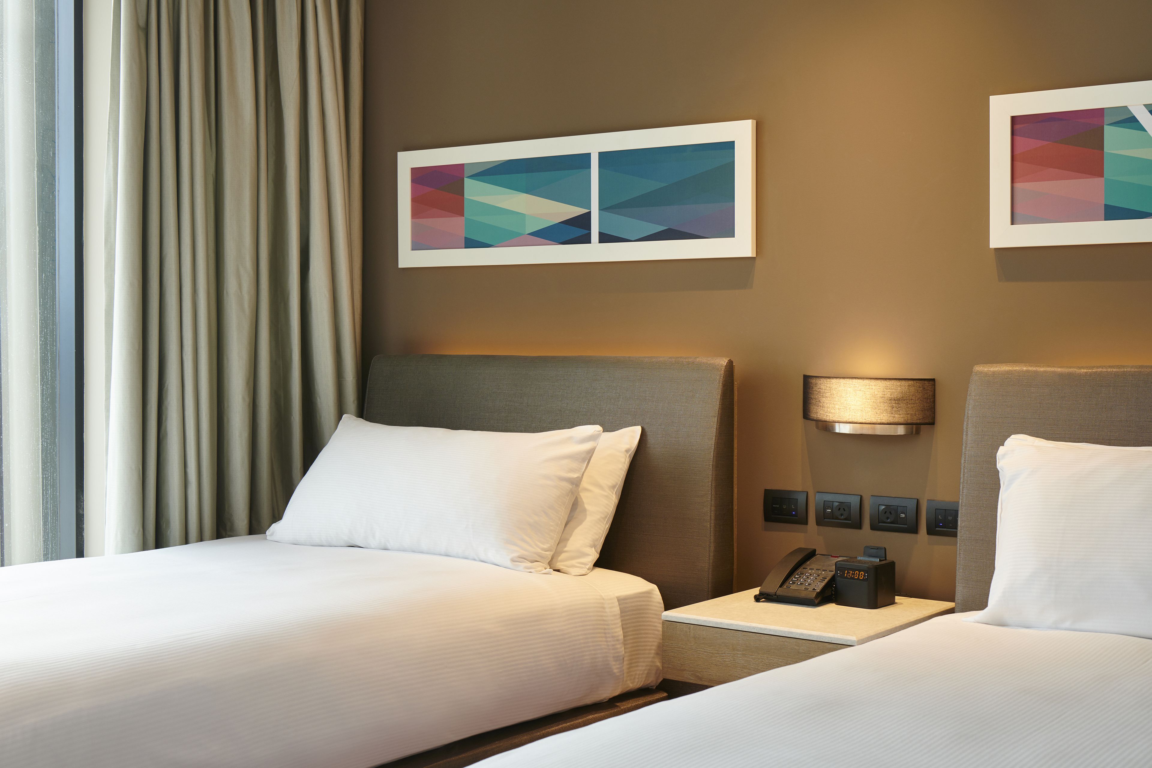 Habitación de hotel con dos camas, una mesita de noche con teléfono y dos lámparas de pared.