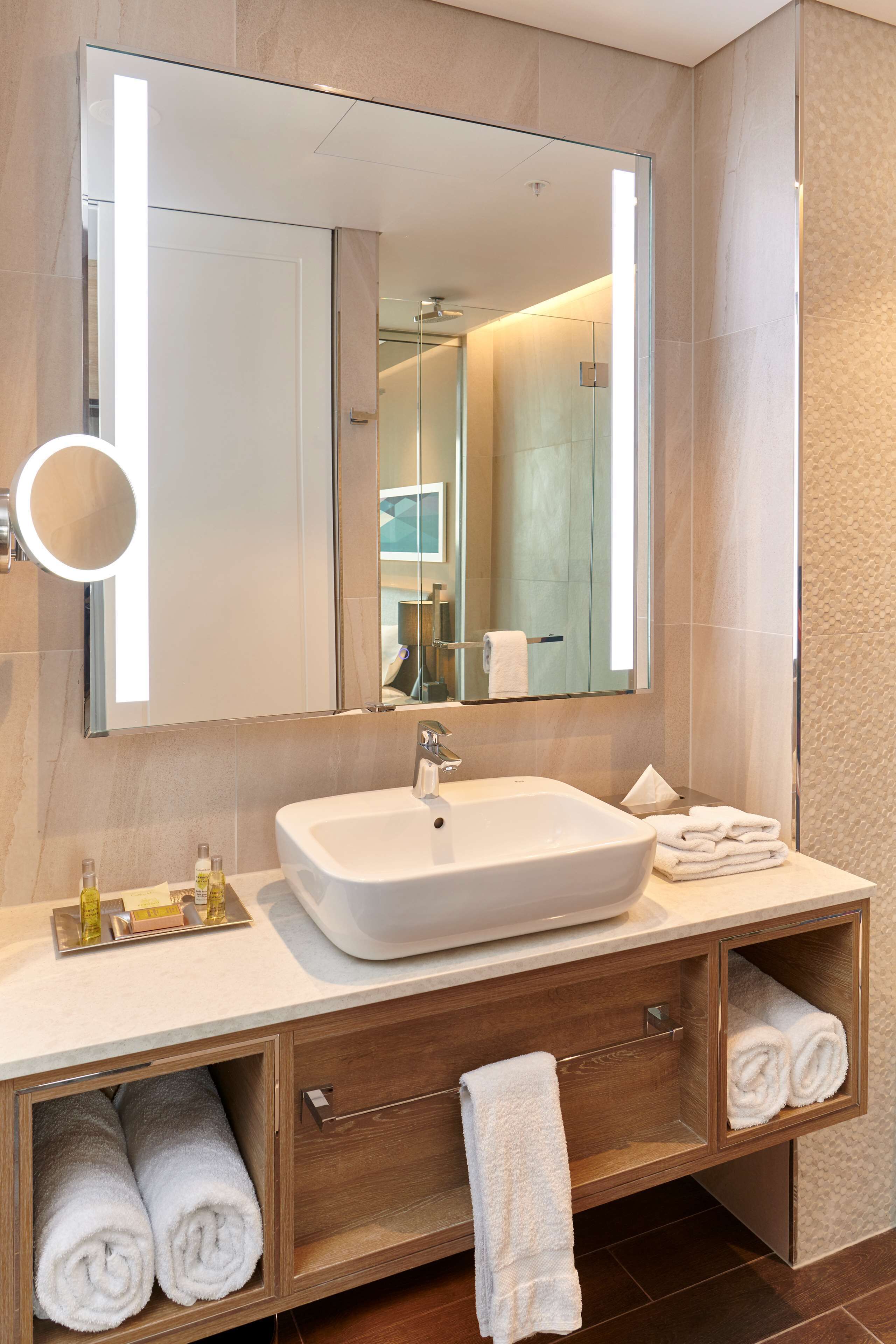 A modern bathroom with a large mirror, a white sink, and wooden cabinets.