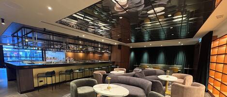 A modern bar area with a bar counter, seating with round tables, and a patterned floor.