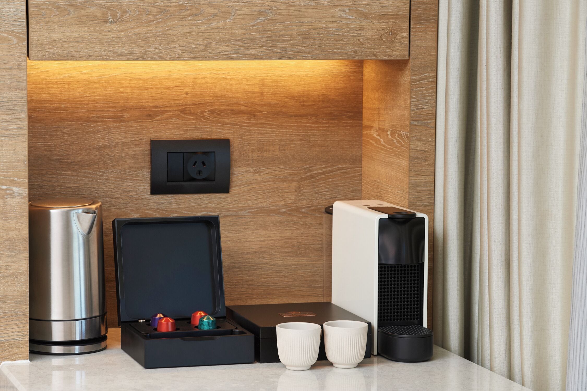 A modern kitchen with a built-in coffee machine, a kettle, and a box with two cups.