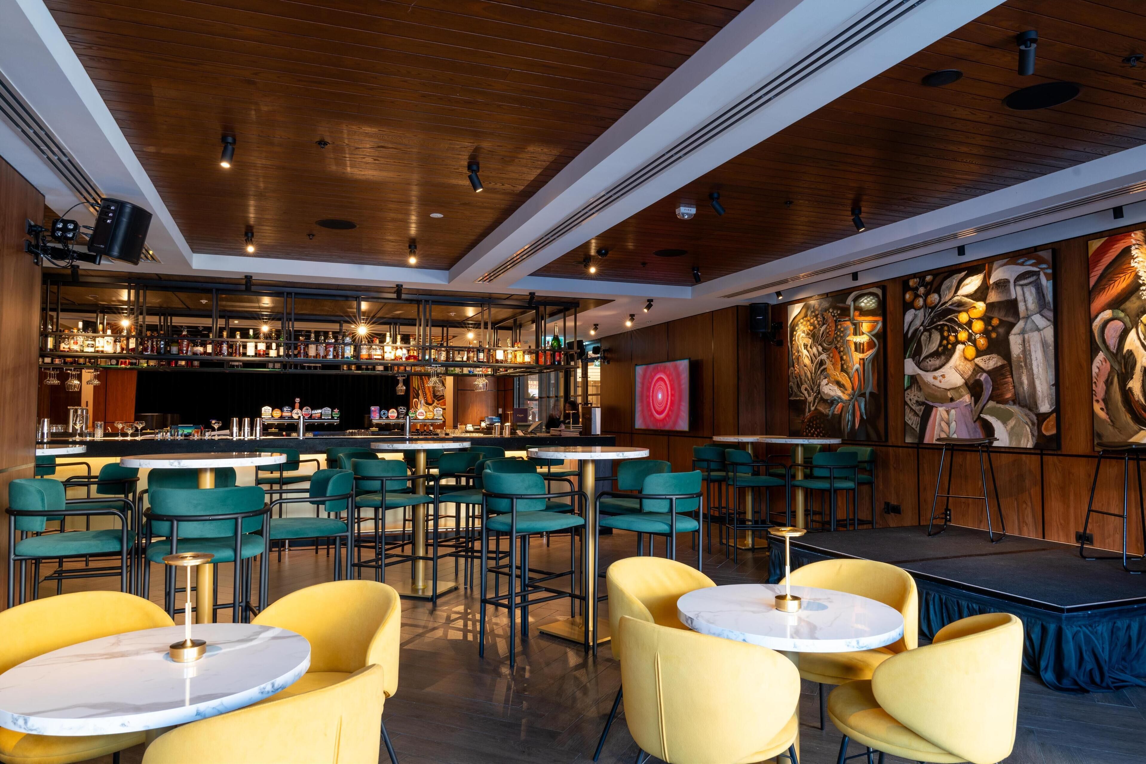 A bar area with multiple seating arrangements, a stage, and artwork on the walls.