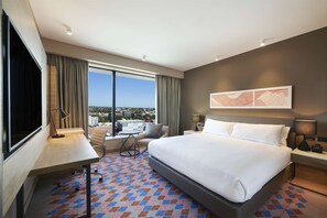 Habitación de hotel con una cama grande, un escritorio, una silla, un televisor y una ventana con vistas a la ciudad.