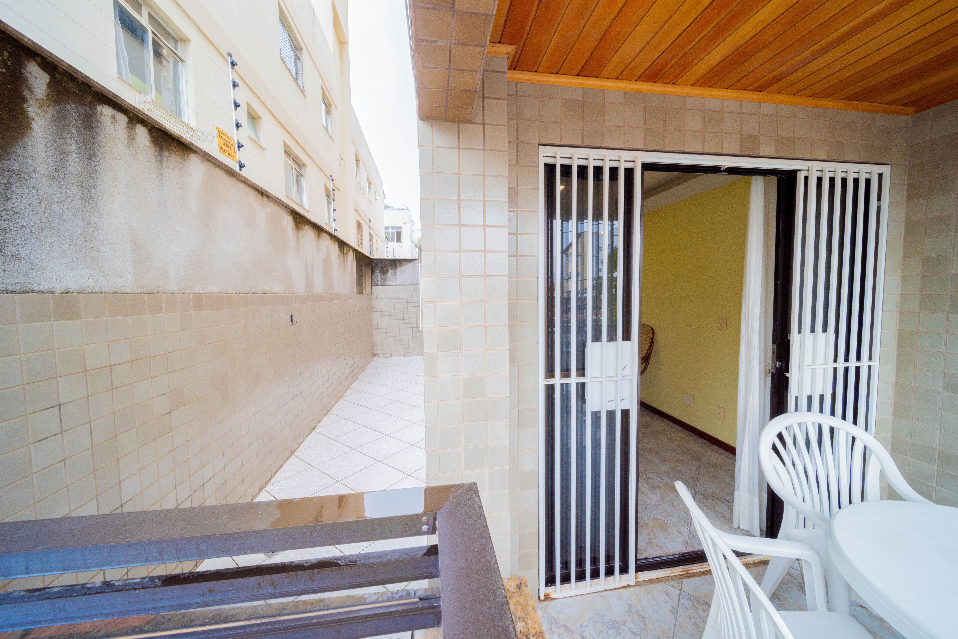 Un espacio al aire libre techado con piso de baldosas, puerta corredera de vidrio y una silla de plástico blanca.