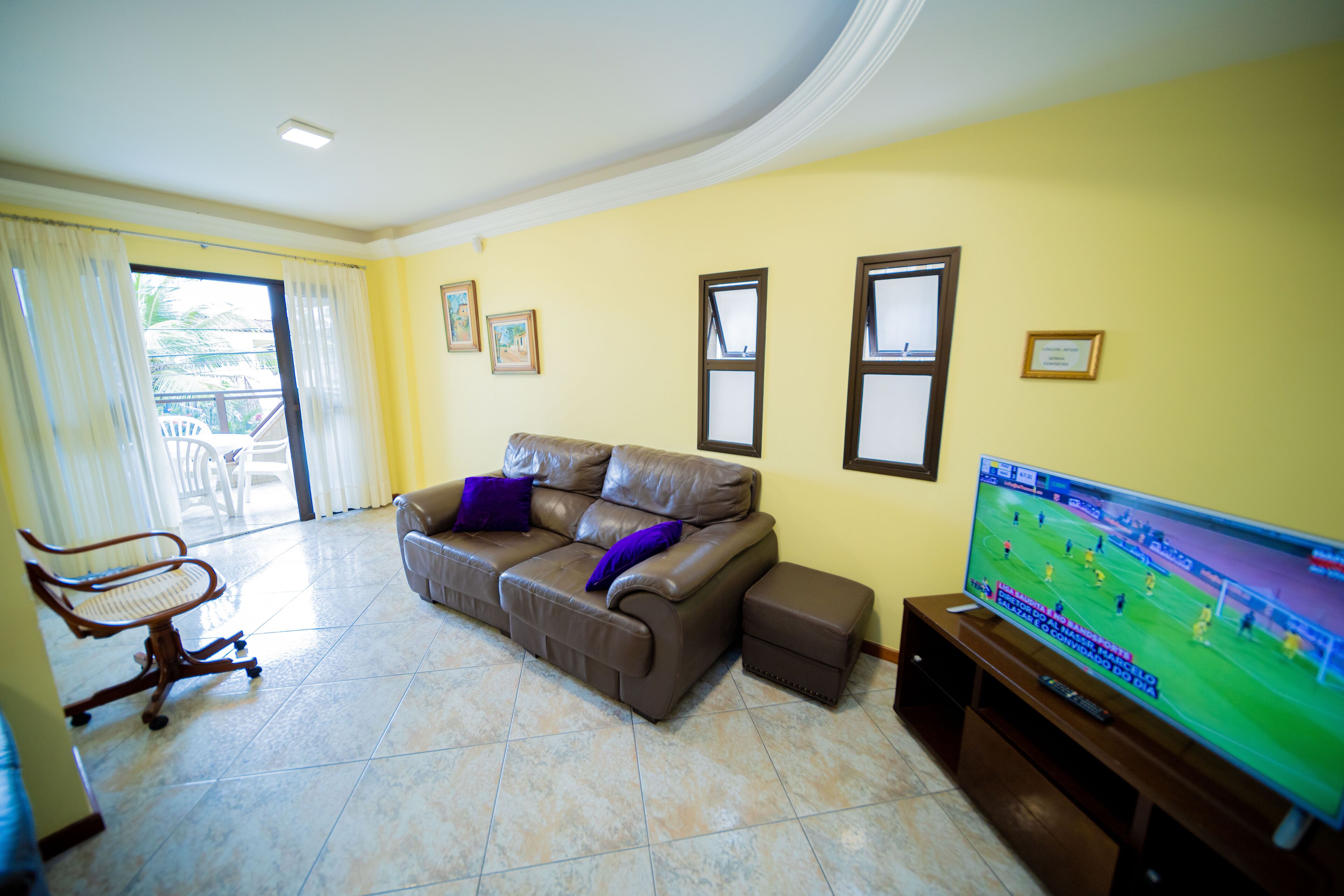 A living room with a brown leather sofa, a television, and a chair.