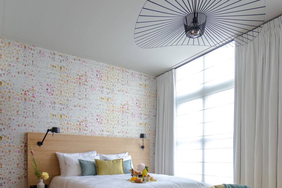 A bedroom with a wooden bed, a yellow armchair, a ceiling fan, and a window with curtains.
