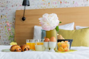 A breakfast setup on a bed with croissants, eggs, juice, and a fruit bowl. - Boutique Hotel Catshuis (Leeuwarden)