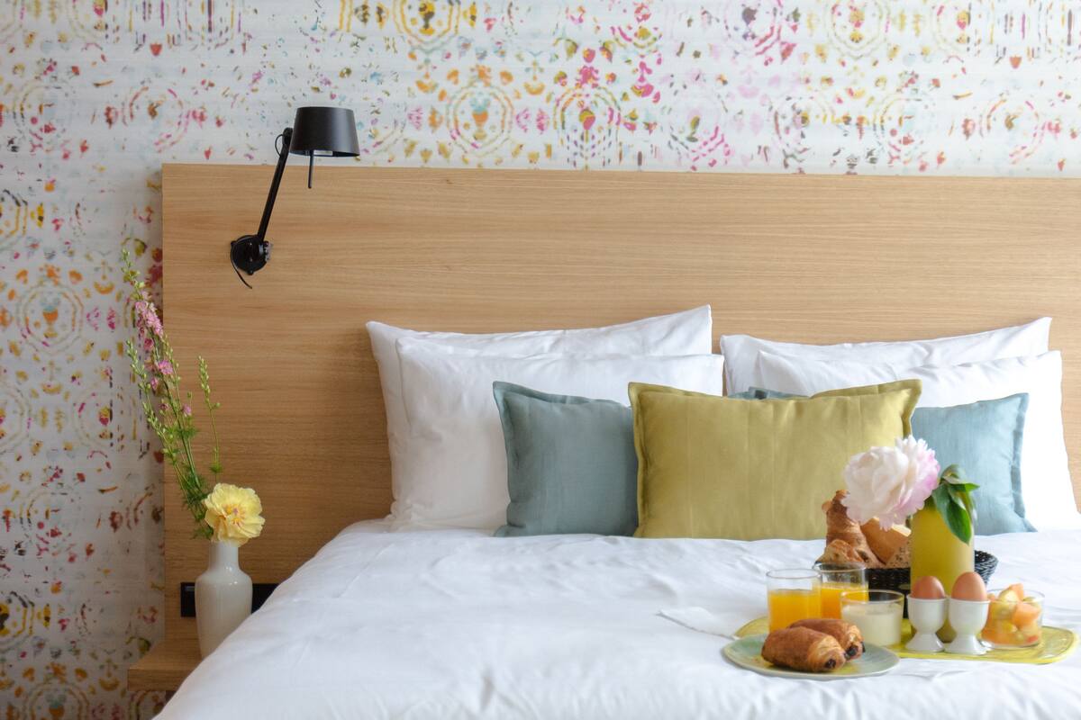 A neatly made bed with a wooden headboard, white bedding, and a breakfast tray with eggs, toast, and juice.