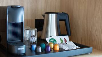 A coffee machine, a kettle, and a tray with coffee capsules and a coffee pod on a wooden surface.
