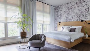 A modern bedroom with a large bed, a grey armchair, a small side table, a potted plant, and a patterned wall. - Boutique Hotel Catshuis (Leeuwarden)