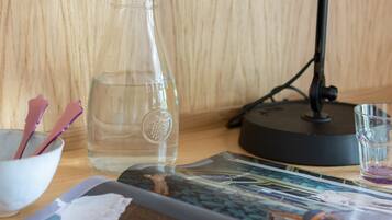 A wooden desk with a clear glass bottle, a black desk lamp, a bowl with purple items, and a magazine.