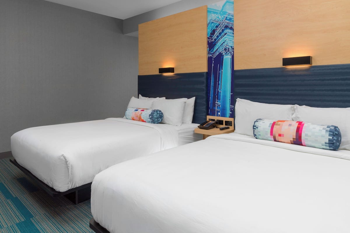 A hotel room with two single beds, a nightstand with a phone and remote control, and a large wall mural.