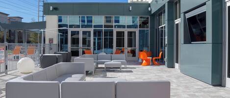 An outdoor seating area with modern furniture, a glass building entrance, and a clear sky.