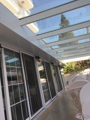 A covered patio with large sliding glass doors, a tiled floor, and outdoor furniture. - Melaike Otel (Foça)