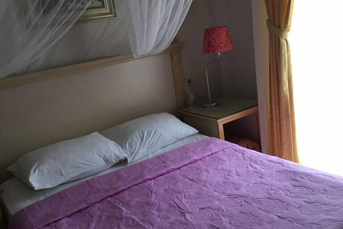Un lit avec une couvre-lit violette, des oreillers blancs et un baldaquin.