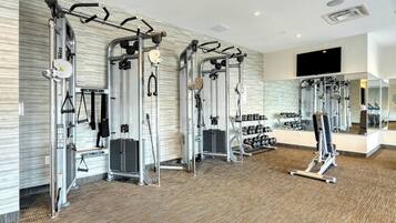 A gym with various exercise machines, a television mounted on the wall, and a mirror reflecting the equipment.