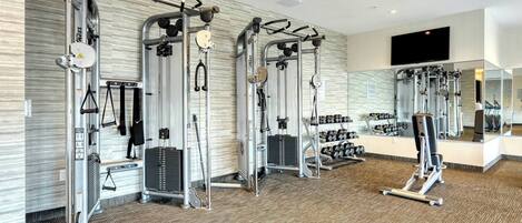 Une salle de sport équipée de divers appareils d’exercice, d’un téléviseur fixé au mur et d’un miroir qui reflète les équipements.