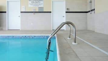 An indoor swimming pool with a no-lifeguard warning sign, a metal pool ladder, and two doors in the background.