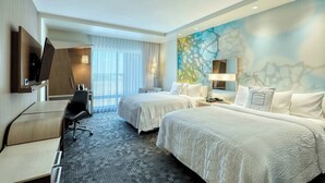 Ein Hotelzimmer mit zwei Betten, einem Schreibtisch, einem Stuhl, einem Fernseher und einem großen Fenster mit Vorhängen.