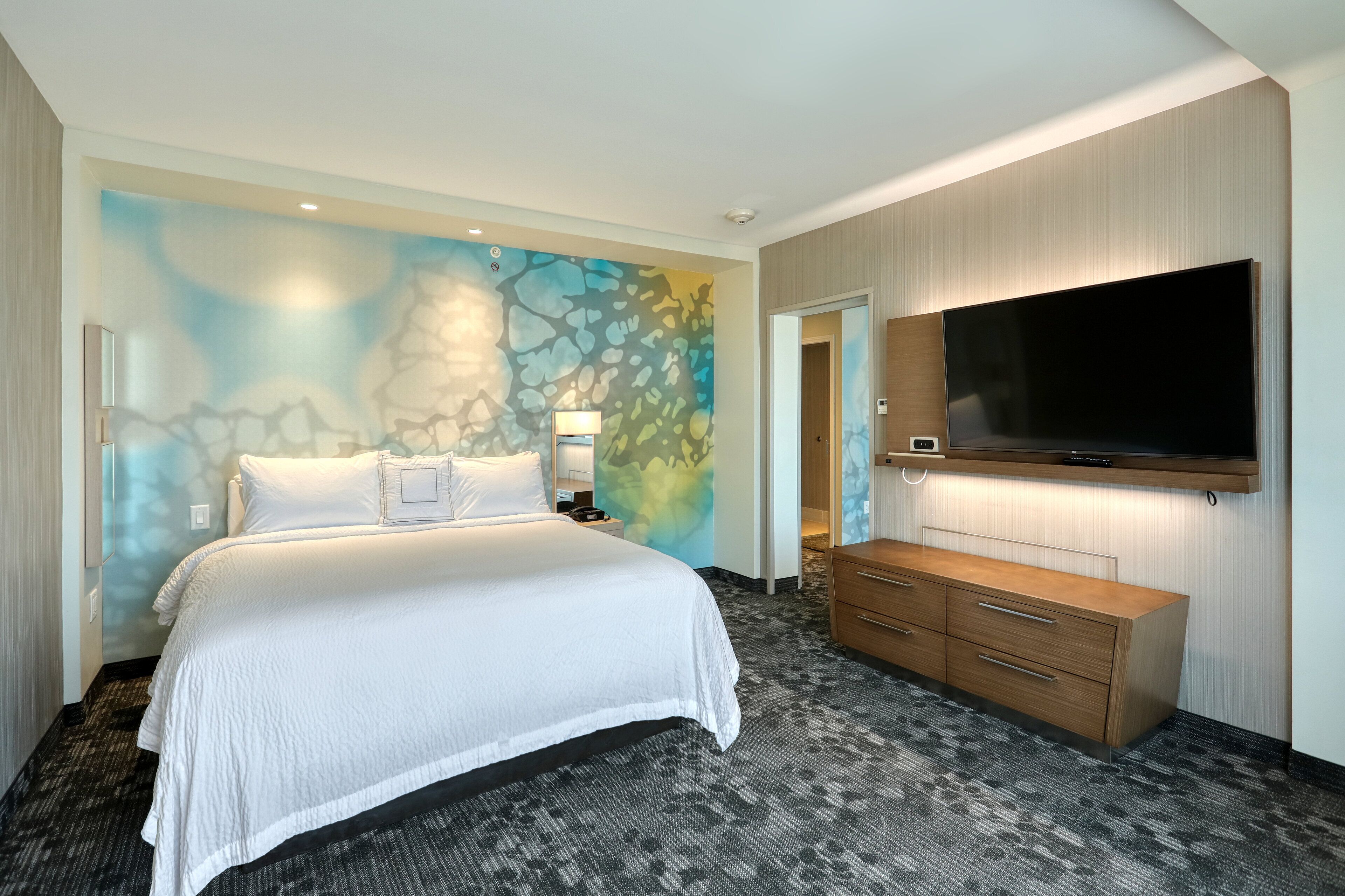 Ein Hotelzimmer mit Bett, Wandfernseher, Kommode und einer einzigartigen Wandmalerei.
