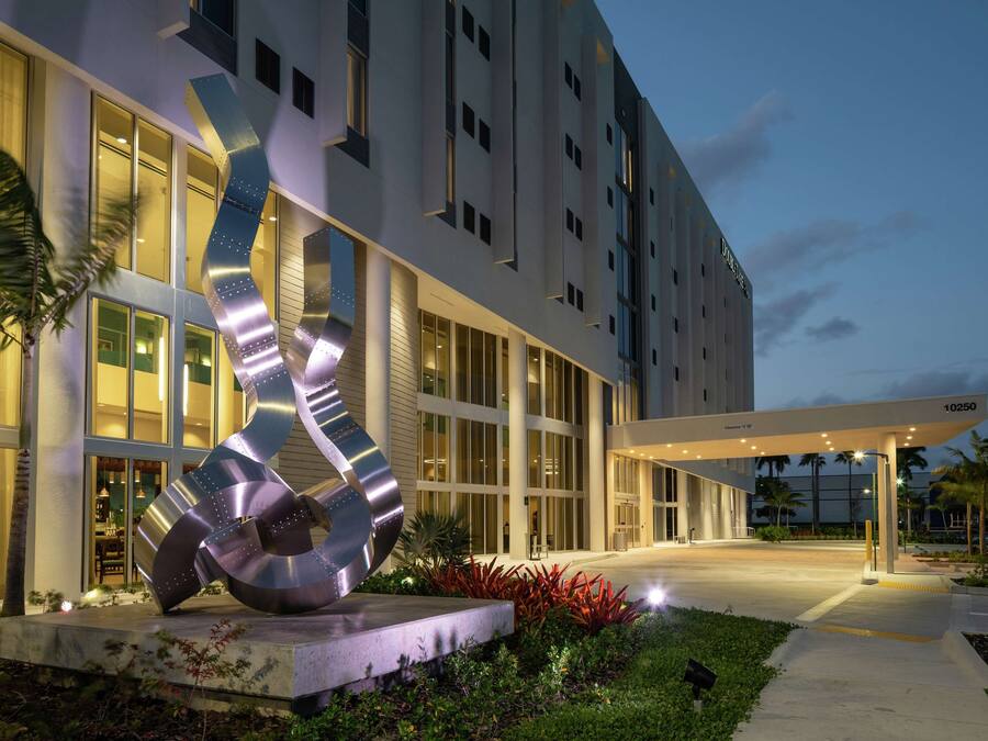 Ein moderner Hotelzugang mit einer großen Metallskulptur, gut beleuchteten Wegen und einem überdachten Außenbereich.