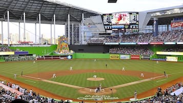 A baseball stadium with a large screen displaying game information, advertisements, and a mascot.