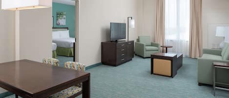 A hotel room with a bed, a TV on a cabinet, a dining table with chairs, a sofa, and a small table with a lamp.