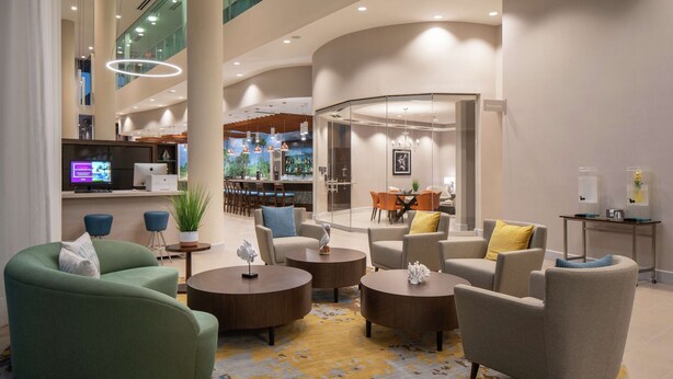 A modern lobby with a curved seating area, a bar, and a dining space. - DoubleTree by Hilton Miami - Doral, FL (Miami)