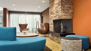 A modern living room with a stone fireplace, blue upholstered furniture, and a floor lamp. - Fairfield Inn & Suites by Marriott Charlottesville Downtown/University Area (Charlottesville)