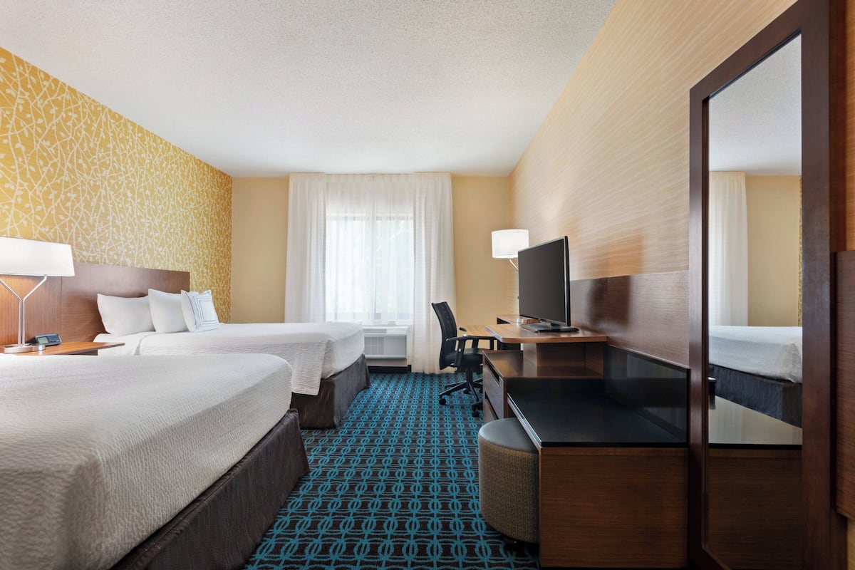 A hotel room with two beds, a desk, a TV, and a mirror.